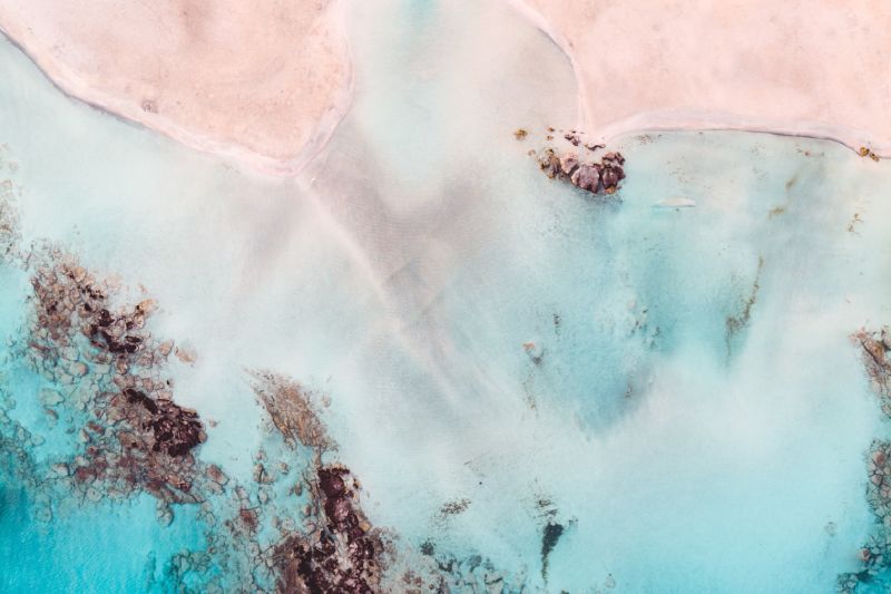 lichtroze strand met azuurblauw water en rotsen